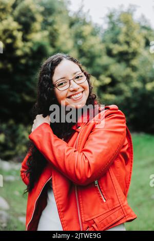 Femme brune souriante, portant une veste en cuir rouge dans la nature. Banque D'Images