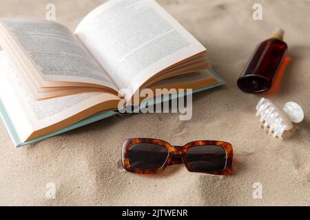 livre, lunettes de soleil et crème solaire sur le sable de plage Banque D'Images