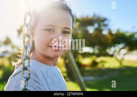 Une journée bien remplie. Portrait d'une petite fille mignonne assise sur une balançoire dans un parc. Banque D'Images