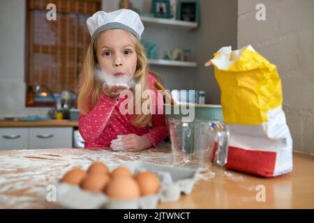 Faire un désordre est la moitié de l'amusement. Une petite fille qui cuit dans la cuisine. Banque D'Images