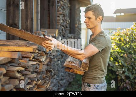 Un homme met le bois entre les mains d'une pile de bois pour une cheminée à la maison. Le concept de chauffage au bois et la crise énergétique Banque D'Images