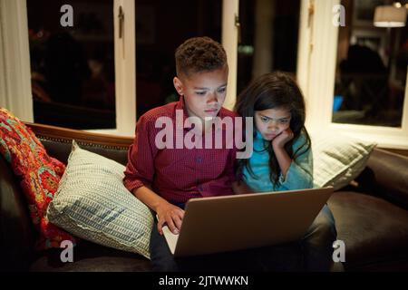 Sommes-nous trop exposer nos enfants à la technologie. Un jeune frère et une sœur utilisant un ordinateur portable après leur coucher à la maison. Banque D'Images