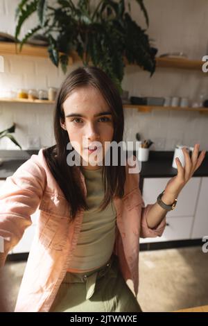 Portrait d'une femme trans non binaire regardant l'appareil photo dans la cuisine à la maison Banque D'Images