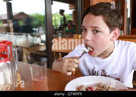 Un enfant mange du varéniki farci de cerises au restaurant Banque D'Images