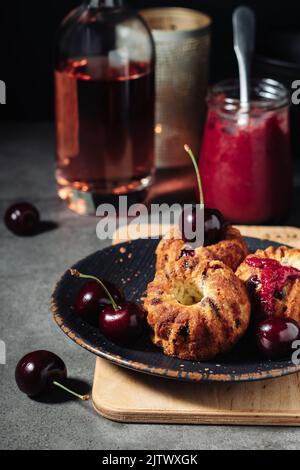 Petits gâteaux avec cerises sur fond sombre. Banque D'Images