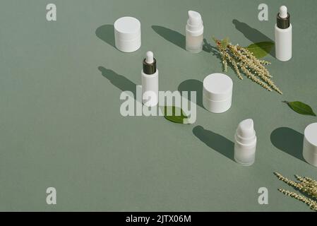 Maquettes blanches d'emballages cosmétiques et de plantes sur fond vert avec espace de copie. Sérum, crème, lotion. Le concept des cosmétiques naturels et de la peau Banque D'Images