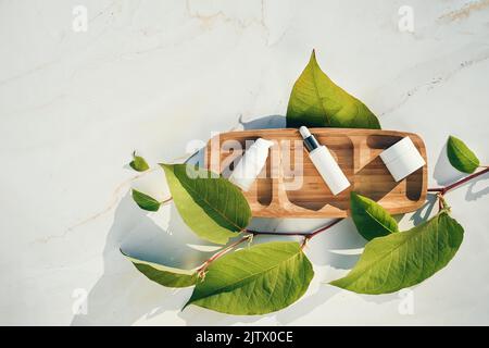 Maquettes blanches d'emballages cosmétiques et de plantes sur un plateau en bois avec des feuilles naturelles. Sérum, crème, lotion. Produit naturel de beauté et de soins de la peau confluent Banque D'Images