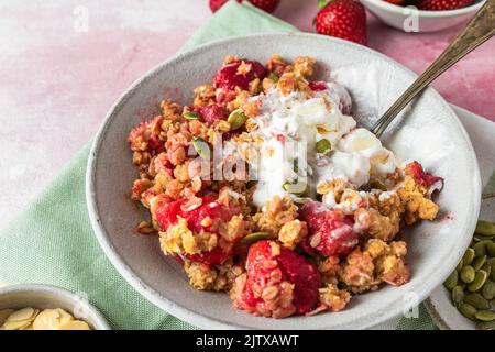 Crumble aux fraises avec glace et amandes dans une assiette avec cuillère sur serviette verte sur fond rose. Petit déjeuner savoureux. Plats délicieux Banque D'Images