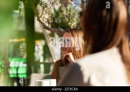 Deux jeunes femmes d'affaires dans un café ayant un sur une réunion. Amis après le travail parlant de gossiping et d'avoir le café à une table de fenêtre avec réflexion Banque D'Images