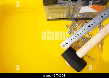 Jeu de tournevis, règle métallique, maillet, vis pour meubles, chevilles en bois dans un récipient jaune Banque D'Images