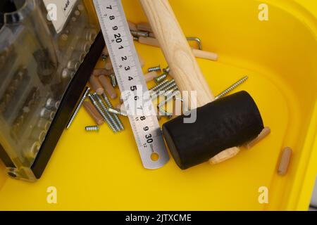 Jeu de tournevis, règle métallique, maillet, vis pour meubles, chevilles en bois dans un récipient jaune Banque D'Images