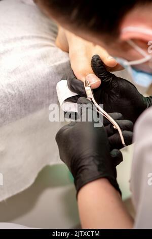 Pédicure professionnelle. Pédicure maître portant des gants en latex coupe les ongles du pied féminin dans le salon de beauté, gros plan Banque D'Images