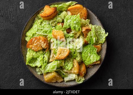 Salade César classique avec croûtons maison croustillants, parmesan et vinaigrette césar dans une assiette sur fond noir. Vue de dessus Banque D'Images