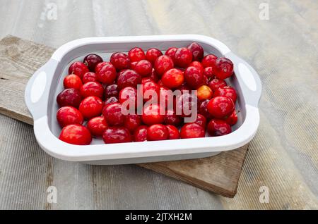 Prunes de cerise rouge mûre sur l'assiette. Fruits juteux sur fond en bois, gros plan. Prune fraîche, plats végétariens Banque D'Images