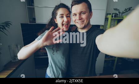 Point de vue prise de vue d'un jeune couple heureux ayant un appel vidéo en ligne avec une caméra de smartphone tout en étant debout dans la cuisine à la maison Banque D'Images