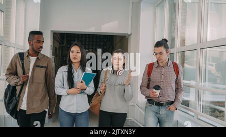 Quatre étudiants masculins et féminins sérieux, concentrés et de différentes origines ethniques, se promeunaient dans un vaste couloir blanc de l'université, en révisant les matériaux avant d'être soumis à un examen difficile Banque D'Images