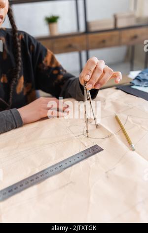 Vue rognée du dessin de designer afro-américain avec boussole sur le motif de couture près du crayon, image de stock Banque D'Images