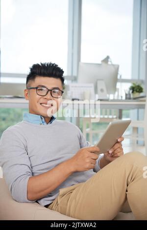 Portrait d'un jeune homme d'affaires assis avec une tablette au bureau Banque D'Images