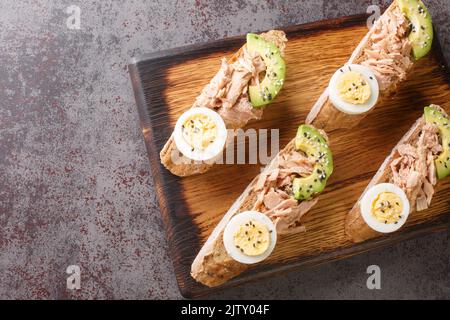 Des sandwichs ouverts avec du thon en conserve, des œufs durs, de l'avocat mûr et des graines de sésame sont servis sur une planche en bois. Vue horizontale du dessus Banque D'Images