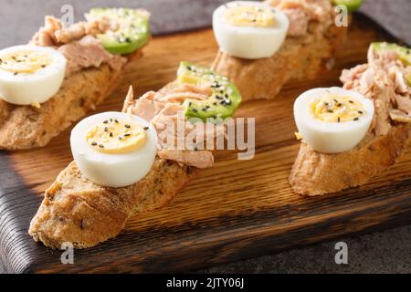 Des sandwichs ouverts avec du thon en conserve, des œufs durs, de l'avocat mûr et des graines de sésame sont servis sur une planche en bois. Horizontale Banque D'Images