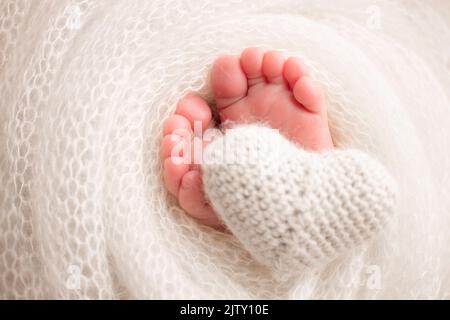 Coeur blanc tricoté dans les jambes d'un bébé. Pieds doux d'un nouveau né dans une couverture. Banque D'Images