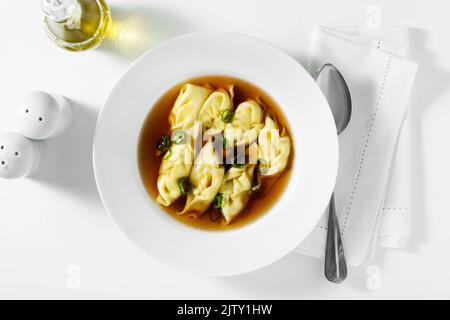 boulettes asiatiques cuites à la vapeur servies dans un bouillon de piment sur une table blanche Banque D'Images