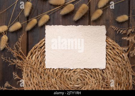Carte vierge et enveloppe sur le platemat à wattLED sur le bois près de la vue de dessus de l'herbe de queue de Hare. Scène boho avec carte papier horizontale. Bohemian ou proche de natur Banque D'Images