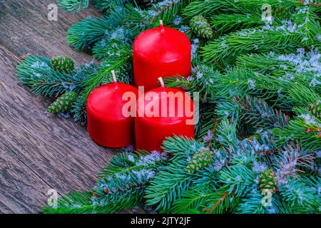 Contexte d'une carte-cadeau. Trois bougies rouges dans des branches de sapin enneigées avec des cônes en gros plan Banque D'Images