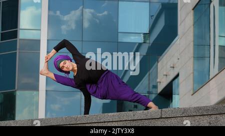 Femme forte dans hijab flexible fille faisant des exercices de yoga sur rue ville bâtiment arrière-plan sport dame se tient dans le côté planche sur une main étire le corps Banque D'Images