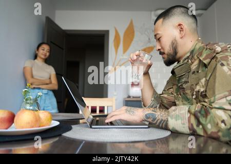 Un jeune homme en uniforme militaire est assis devant un ordinateur portable Banque D'Images