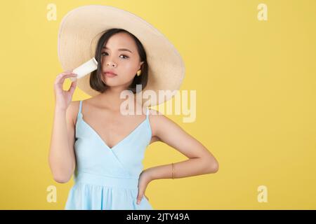 Belle jeune femme avec écran solaire debout sur fond jaune Banque D'Images