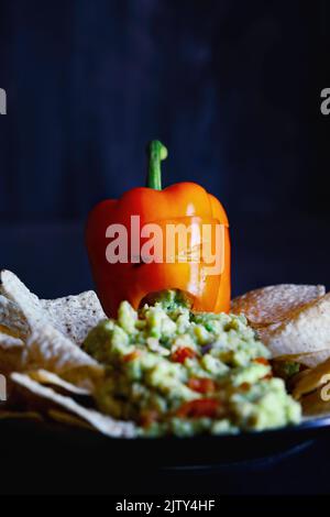Poivron orange bourré coloré en tant que monstre avec une face coupée sculptée dans un citrouille d'Halloween Jack O'Lantern qui lance une guacamole Banque D'Images