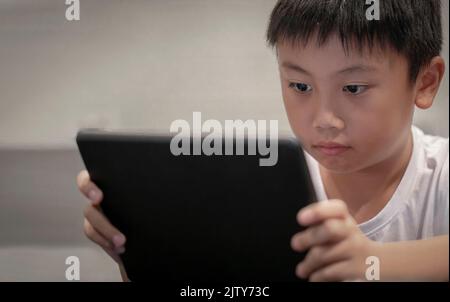 Un garçon asiatique jouant au jeu sur une tablette numérique à la maison , des enfants regardant des dessins animés sur un taplet numérique ou un smartphone Banque D'Images