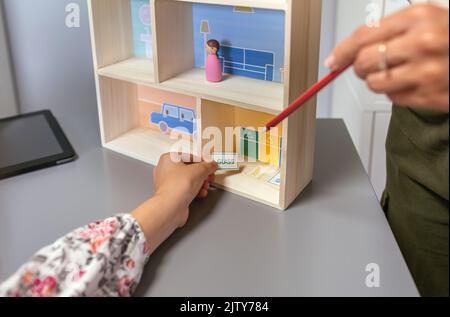 Professeur méconnaissable enseignant le recyclage avec une maison de jouets à une étudiante dans une classe d'écologie Banque D'Images