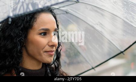 Portrait insouciante belle femme heureuse femme hispanique fille longue sombre cheveux bouclés tenant un parapluie transparent debout dans la ville Banque D'Images