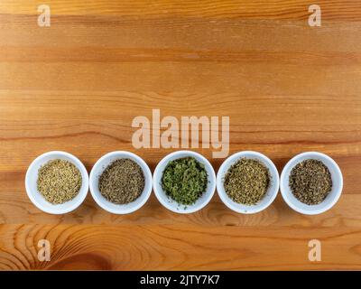 Herbes séchées pour la cuisine méditerranéenne dans des bols blancs sur fond de table en bois Banque D'Images