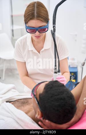 Cosmétologue spécialisé traitant la zone sous les bras du client mâle avec laser Banque D'Images