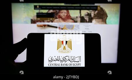 Personne tenant un smartphone avec le logo de l'autorité monétaire Central Bank of Egypt (CBE) à l'écran devant le site Web. Mise au point sur l'affichage du téléphone. Banque D'Images