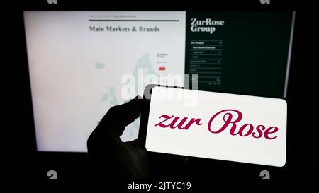 Personne tenant un smartphone avec le logo de la société suisse de pharmacie Zur Rose Group AG à l'écran devant le site. Mise au point sur l'affichage du téléphone. Banque D'Images