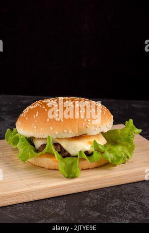 Hamburger avec patty de bœuf sur une assiette en bois sur fond sombre Banque D'Images