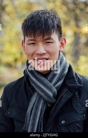 Portrait en gros plan d'un jeune Chinois debout à l'extérieur dans la nature à Northumberland, dans le nord-est de l'Angleterre, en automne. Il sourit tout en looki Banque D'Images
