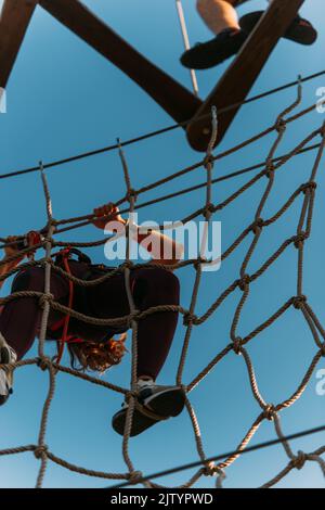 Femme accrochée au mur de cordes essayant de terminer le parcours dans le parc d'aventure Banque D'Images