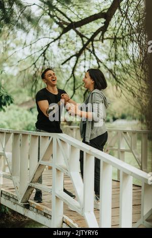 Beau couple qui se secoue et rit en se tenant sur le pont blanc dans le parc Banque D'Images