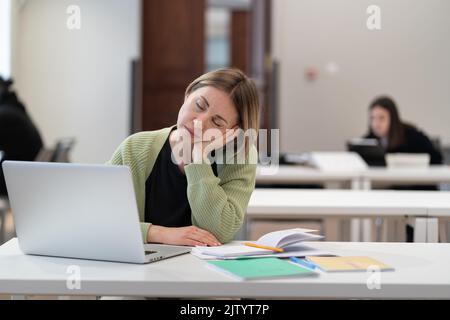 Exténué fatigué femme d'âge moyen étudiant s'endormant en étudiant à la classe d'éducation des adultes Banque D'Images