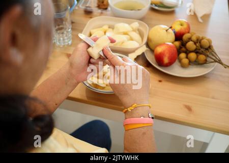 La femme asiatique senior épluchant des fruits dans le plat. Banque D'Images