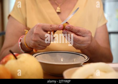 La femme asiatique senior épluchant des fruits dans le plat. Banque D'Images