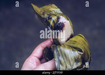 Gros plan de la main tenant délicieux gâteau de riz collant avec saveur de chocolat enveloppé dans la feuille de banane AKA ibus, ibo, suman, ou bourgeon. Point de vue personnel Banque D'Images