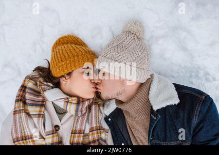 heureux couple embrassant couché sur la neige en hiver Banque D'Images