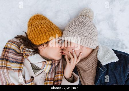 heureux couple embrassant couché sur la neige en hiver Banque D'Images