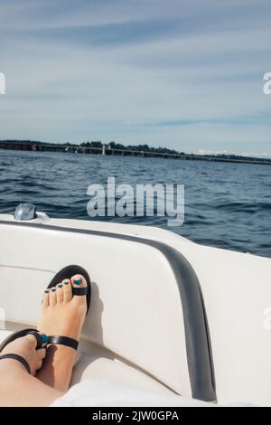 Pieds avec crapauls bleus et sandales à bout noir reposant sur un arc de bateau dans le lac Banque D'Images